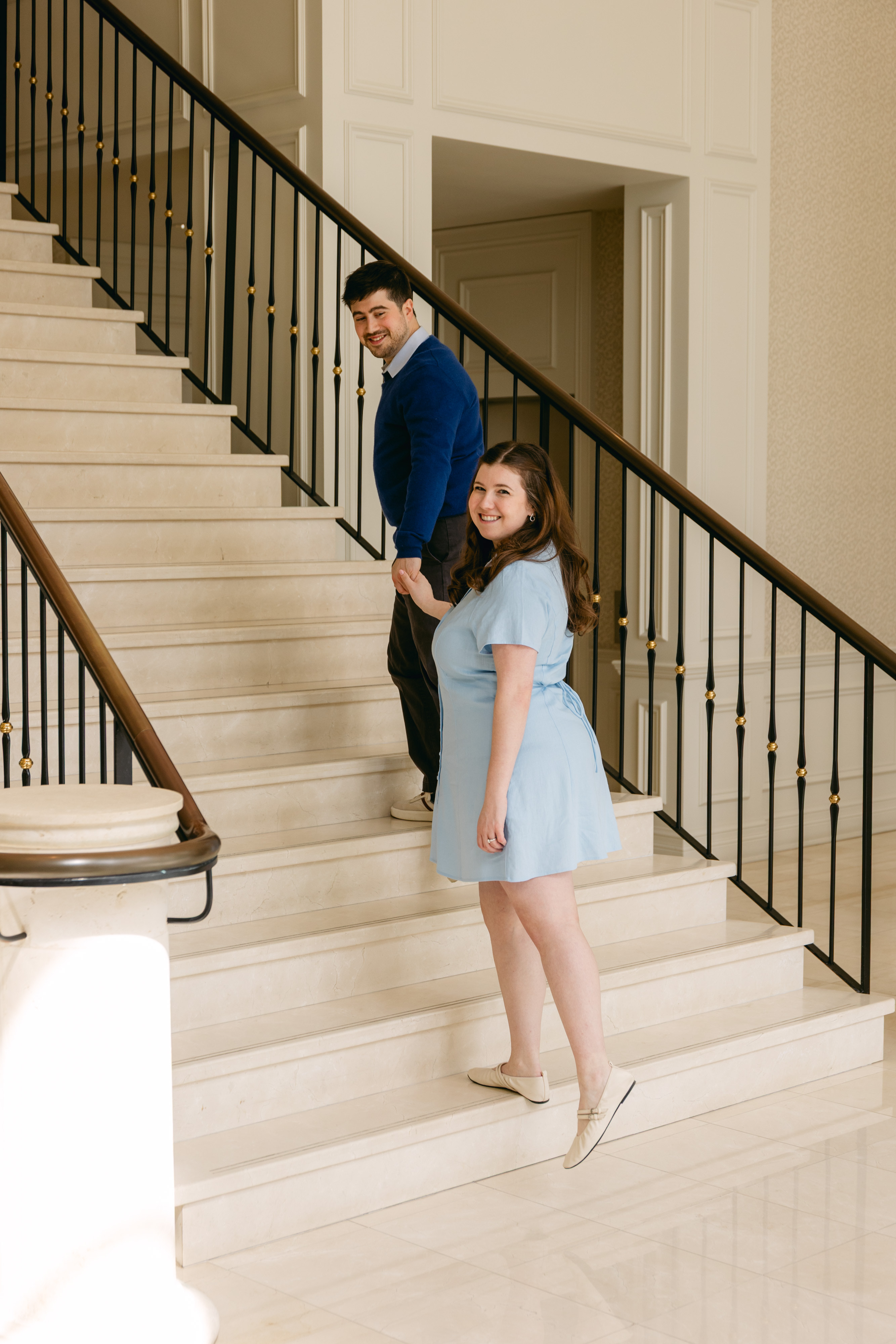 Hailey and Jessie holding hands on an elegant indoor staircase.